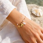 siknakit-zlata-zapestnica-aegean-pearl-charms-closeup-na-roki-bela-tkanina